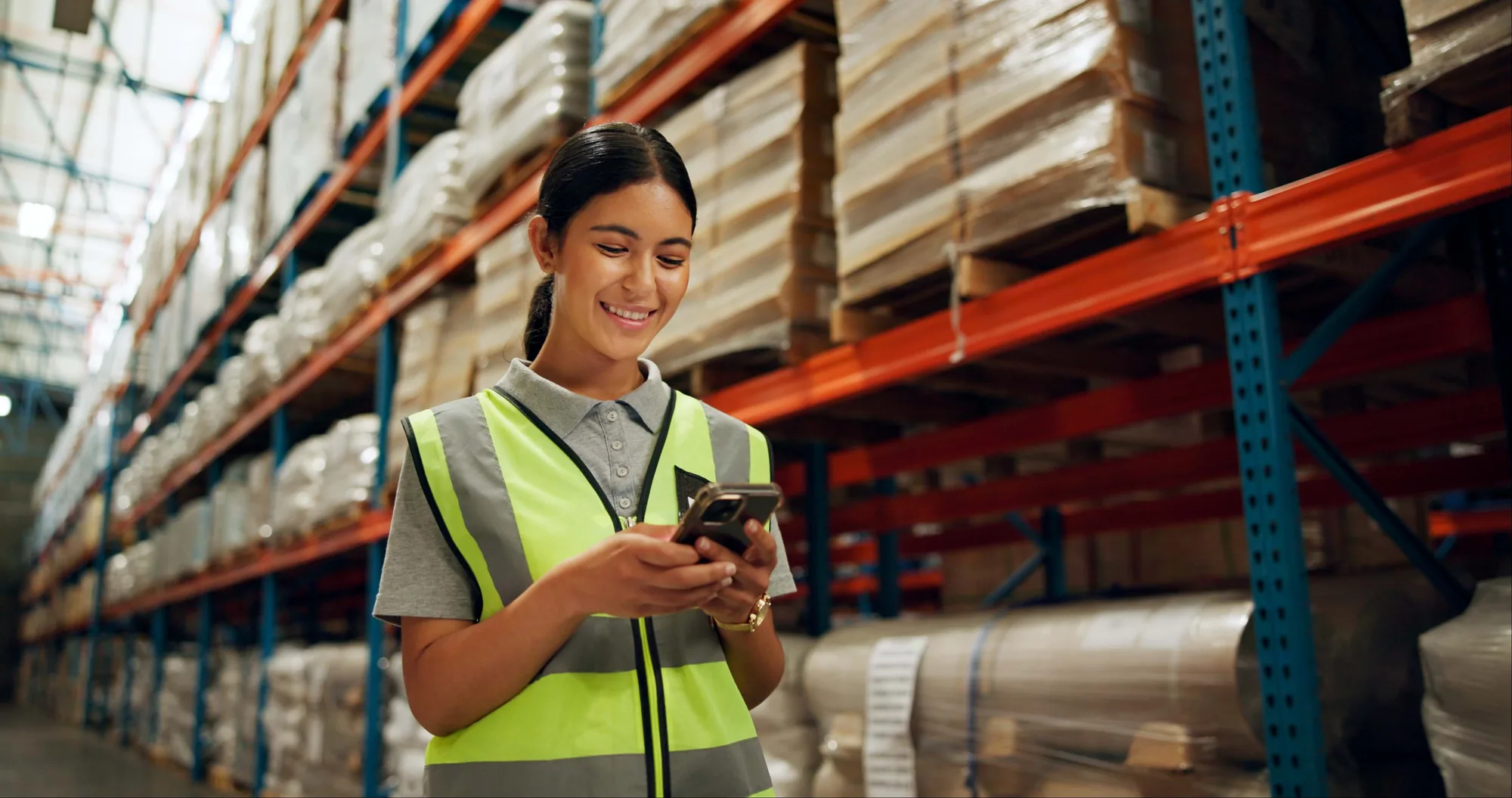 Transport industry member in a safety vest checking her account on her phone in a warehouse
